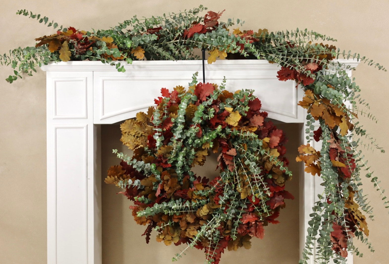 Decorative wreath and garland on a white fireplace mantel against a beige wall.
